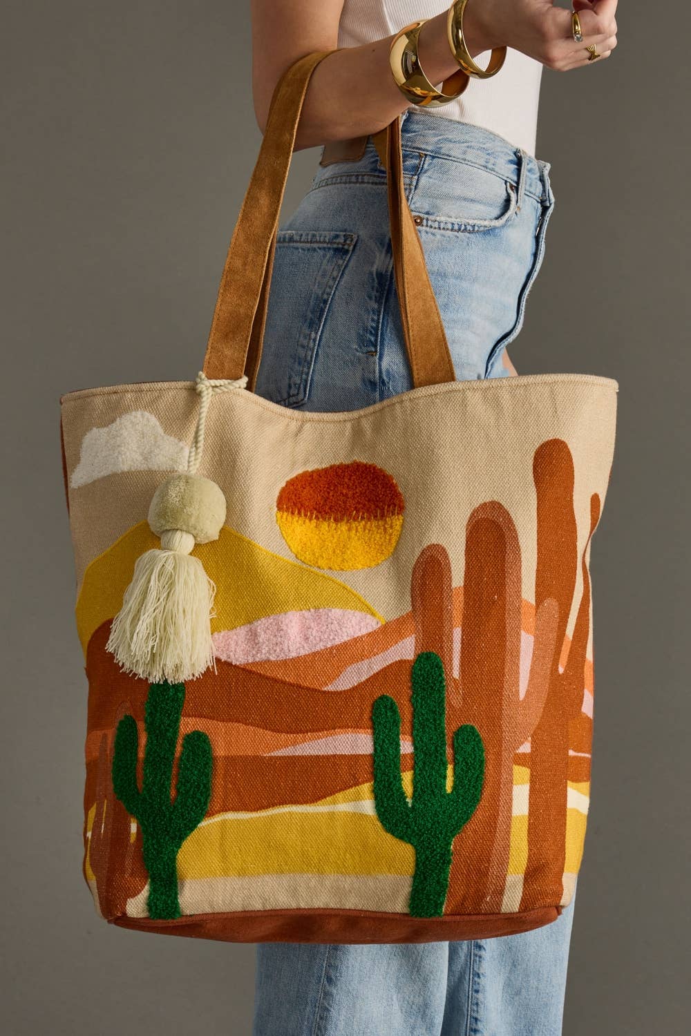 Tote bag with desert design and tassel held by a person wearing jeans.