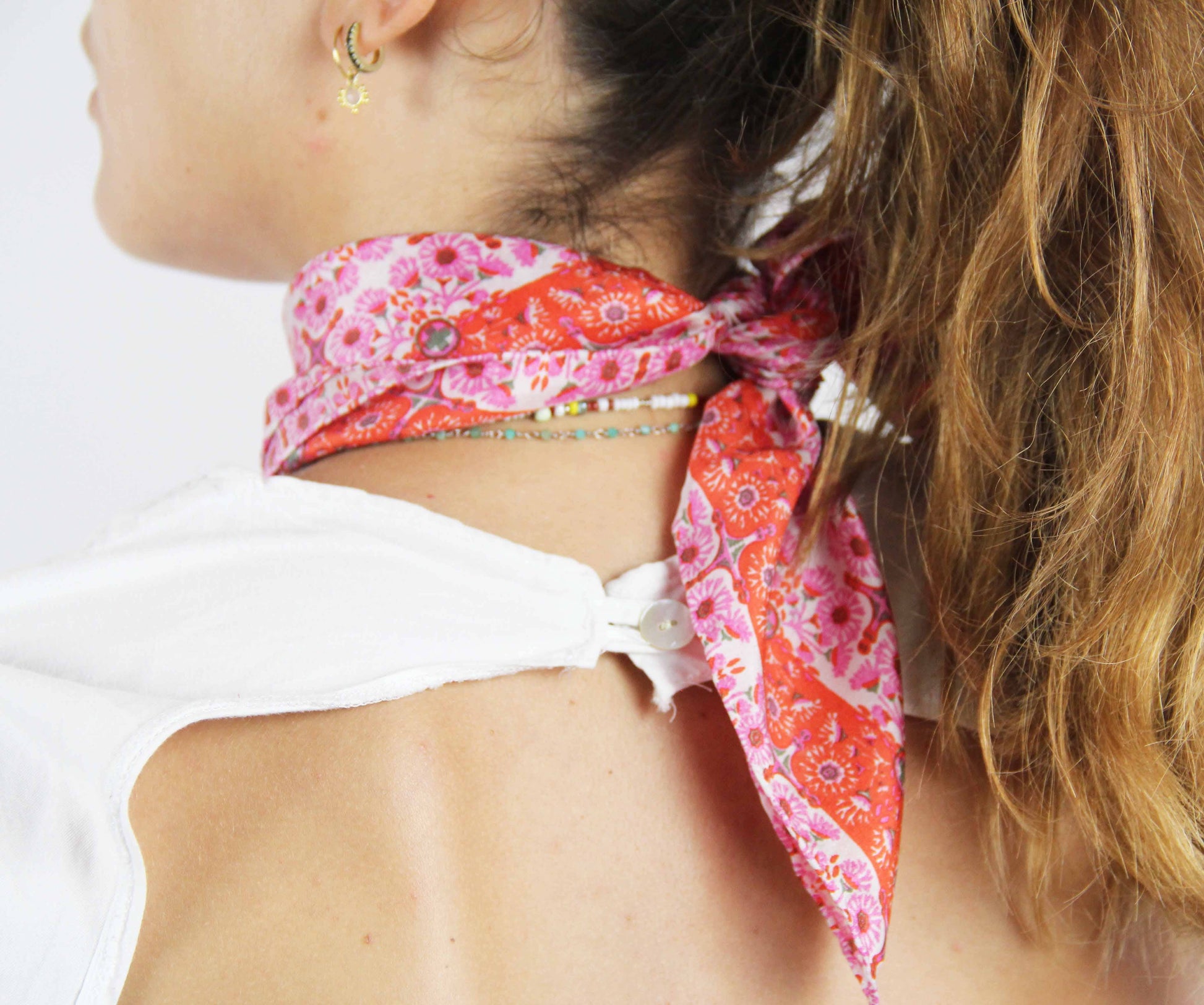 Woman wearing a pink floral headscarf with a white top on a plain background