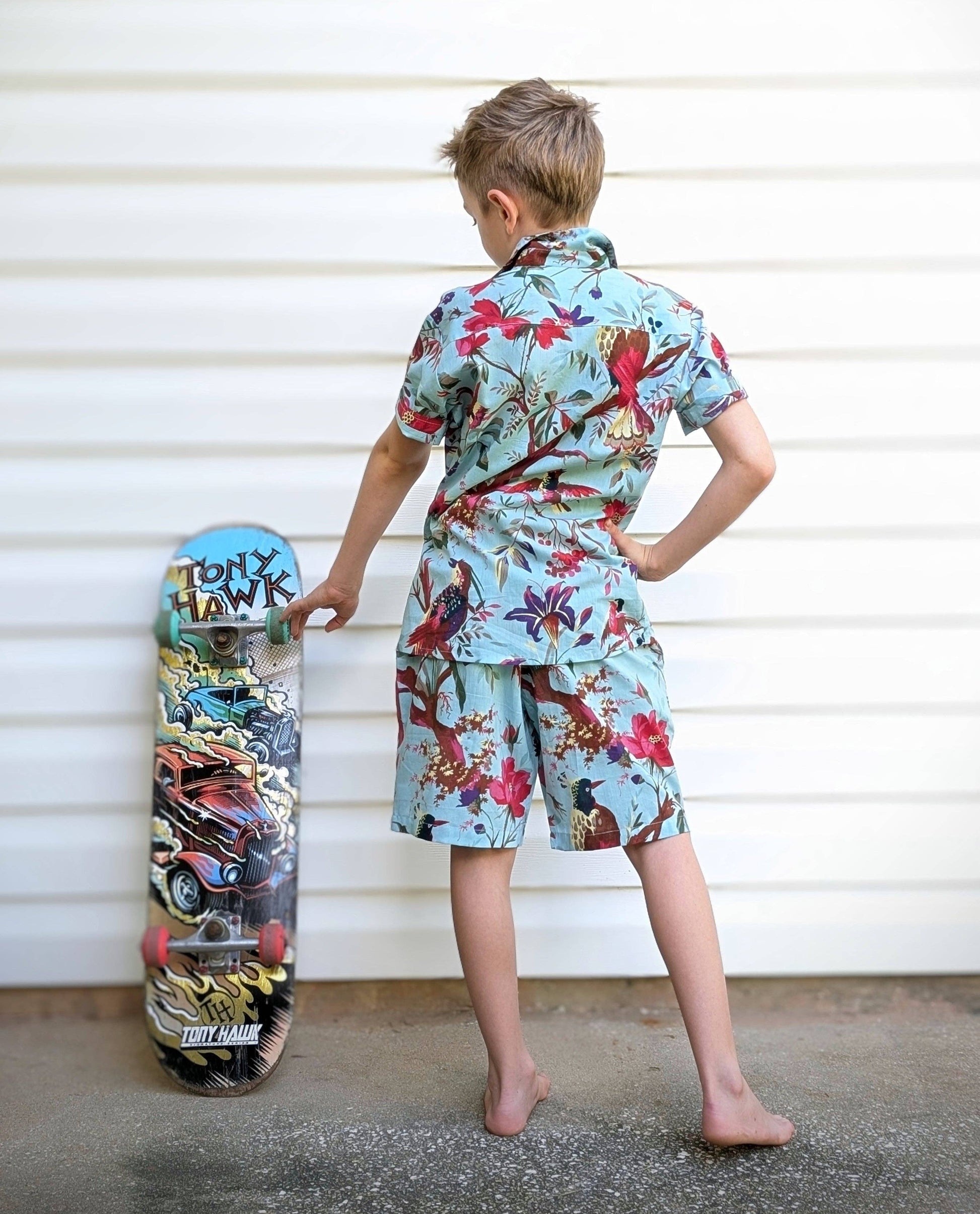 Child wearing a colorful outfit holding a skateboard against a white wall.