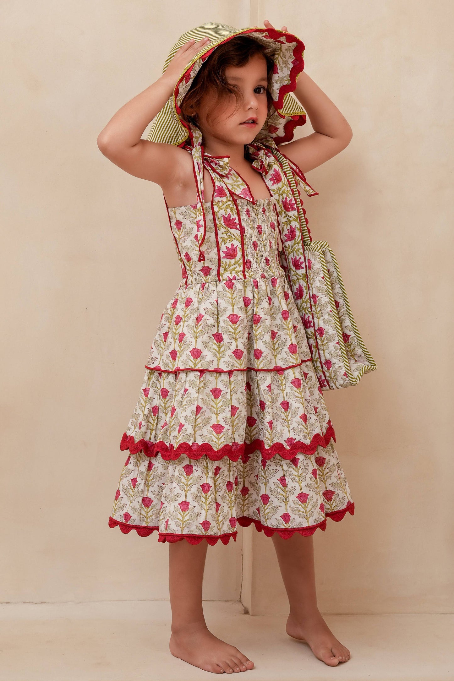 Young girl wearing a floral dress and sun hat against a beige background