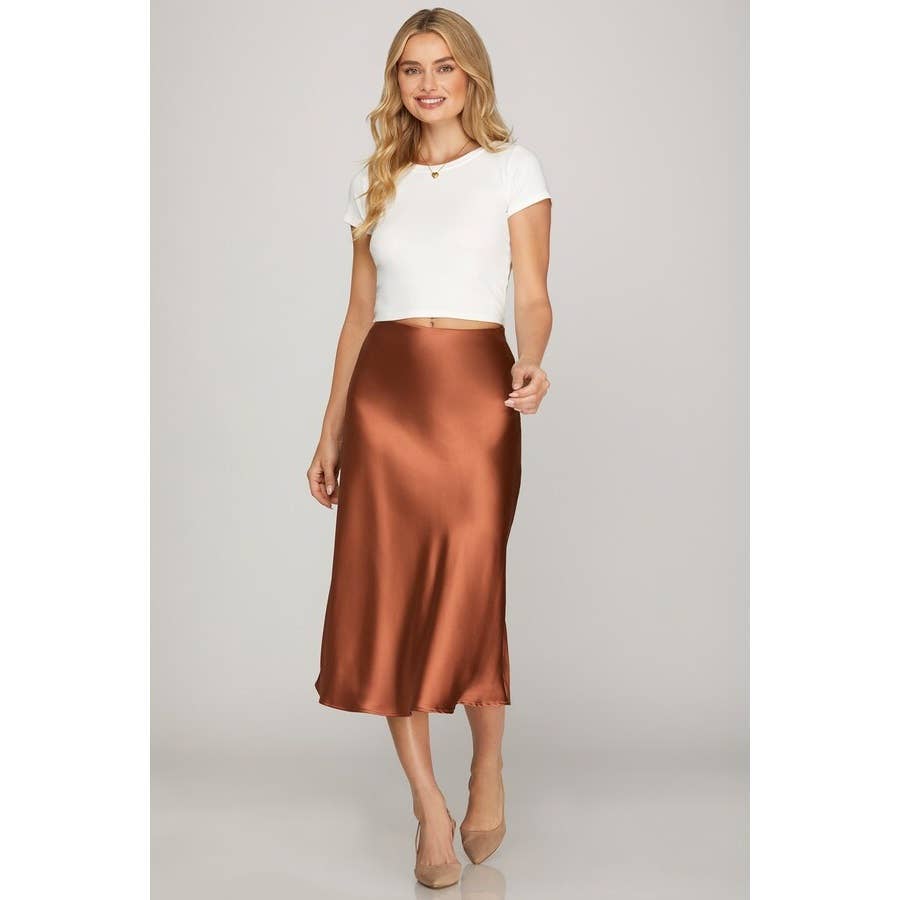 Woman wearing a white top and copper satin skirt on a plain background