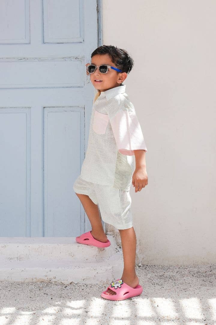 Child wearing sunglasses and a white outfit with pink shoes standing on steps.