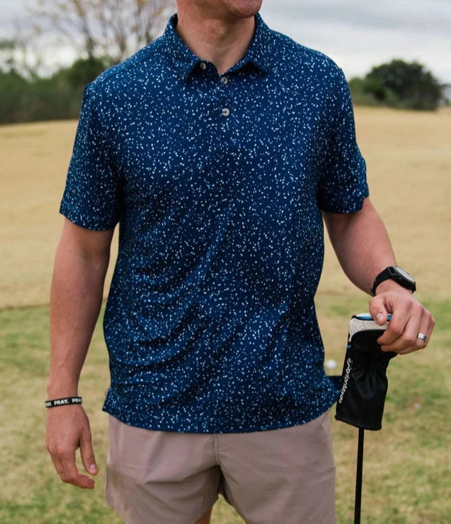 model wearing navy speckled polo with hat and shorts at golf course