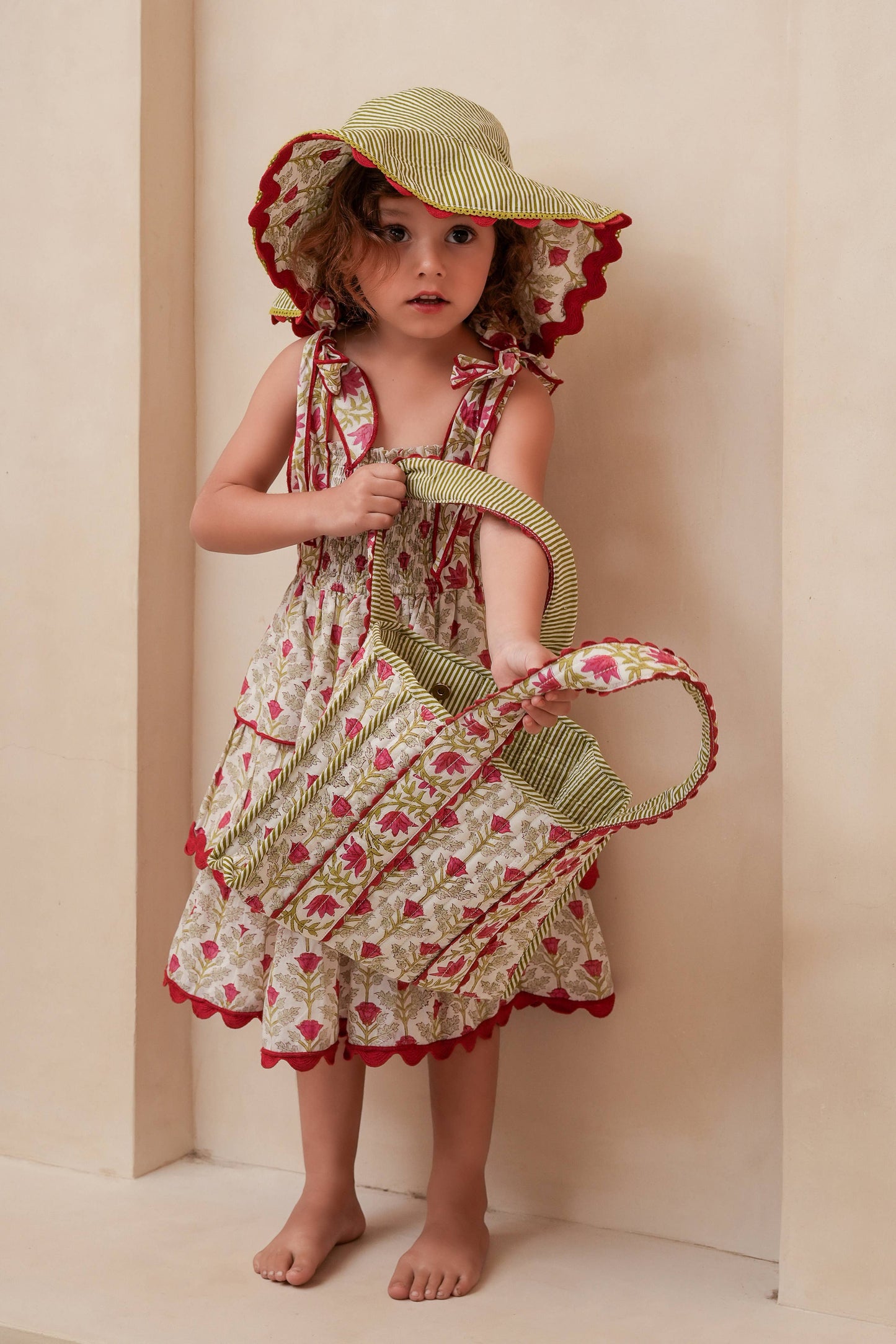 Child wearing a floral dress and sun hat holding a parasol against a beige background