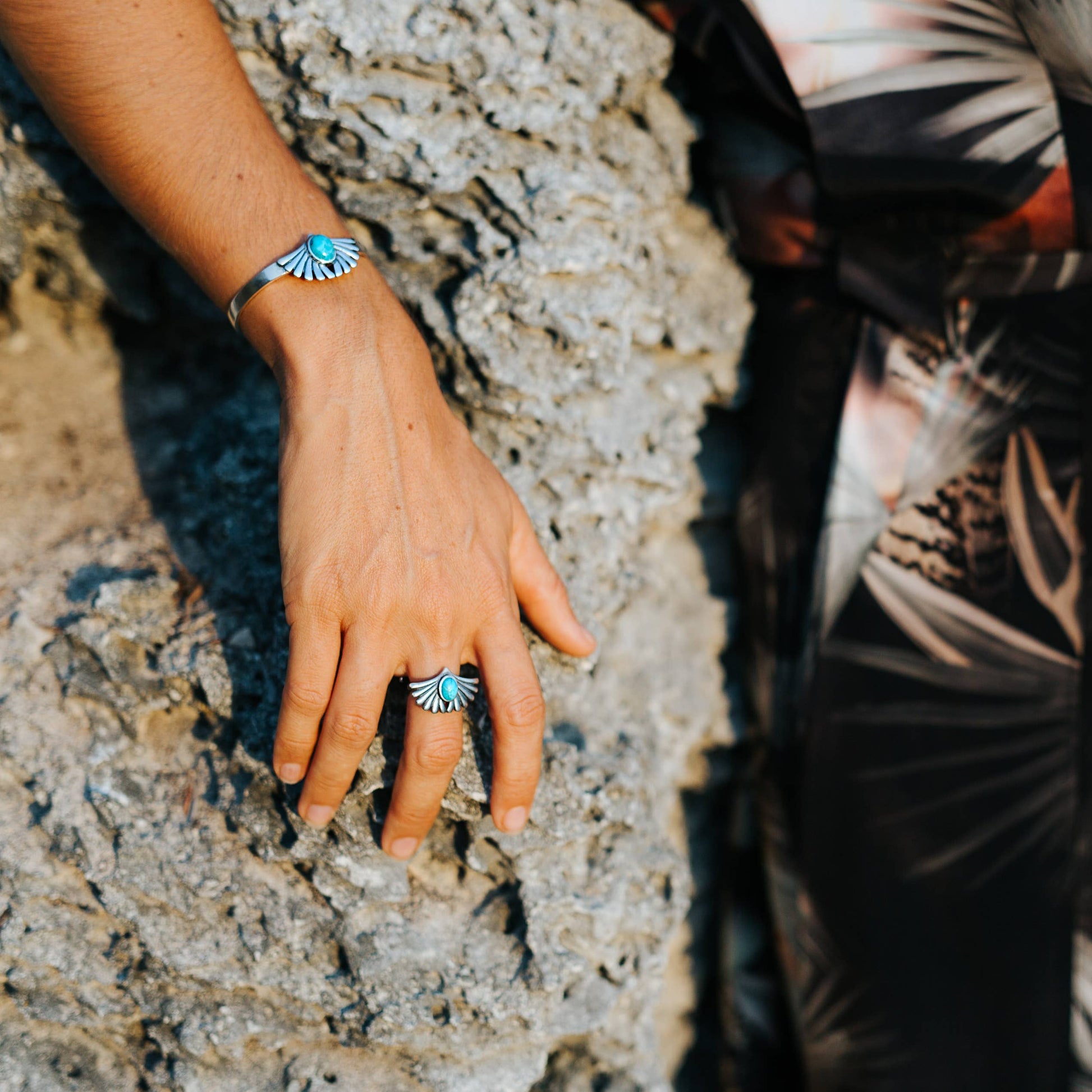Hand with turquoise rings on a textured stone surface