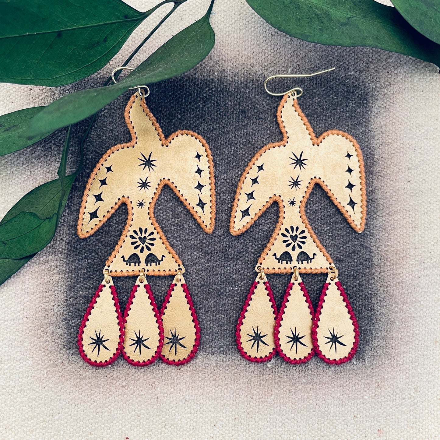 Pair of earrings with geometric design on a textured surface with leaves in the background