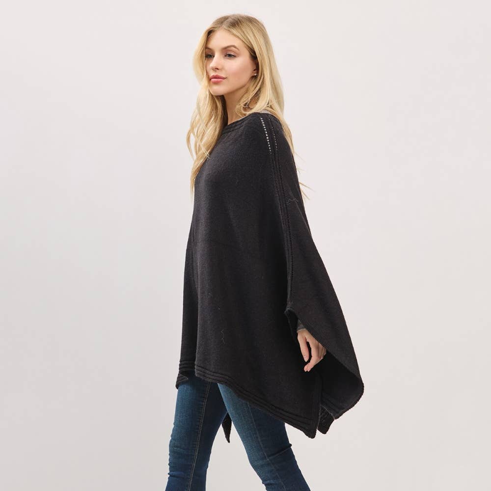 Woman wearing a black poncho and blue jeans on a white background