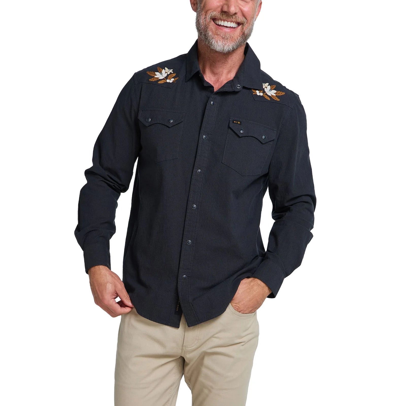 A man wearing a dark western-style button-up shirt with embroidery details on the shoulders and beige pants, photographed against a plain white background.