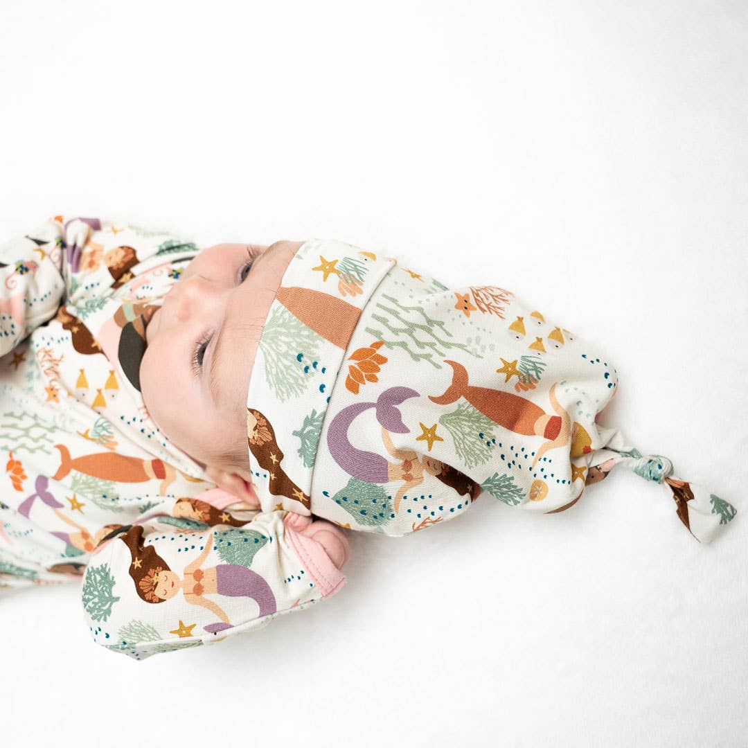 Baby wrapped in a colorful blanket with mermaid pattern on a white background