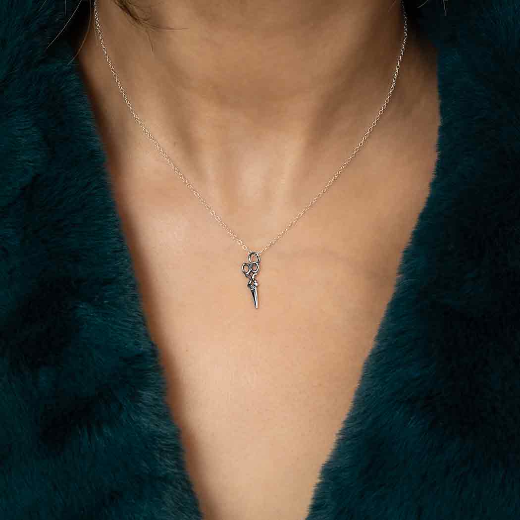 Necklace with a small pendant worn by a person in a green fur garment.
