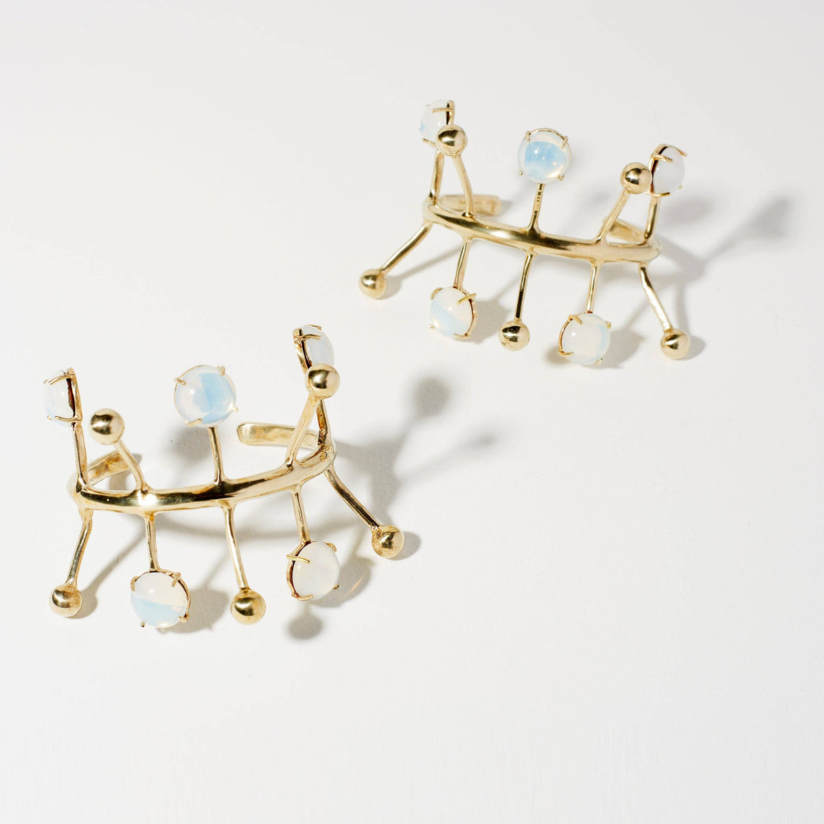 A pair  gold-toned geometric cuff bracelet featuring five round, milky white gemstone accents set in gold, displayed on a clean white background.