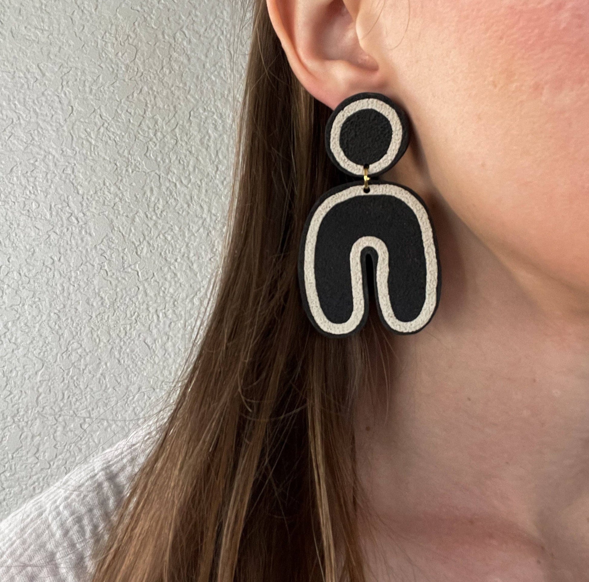 Black and white Post and dangle earrings with round port and u shaped dangle. Close up On brown haired model