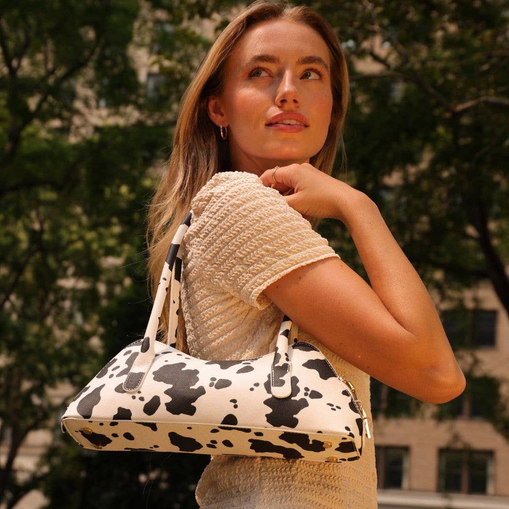 Woman holding a cow print handbag outdoors with blurred background