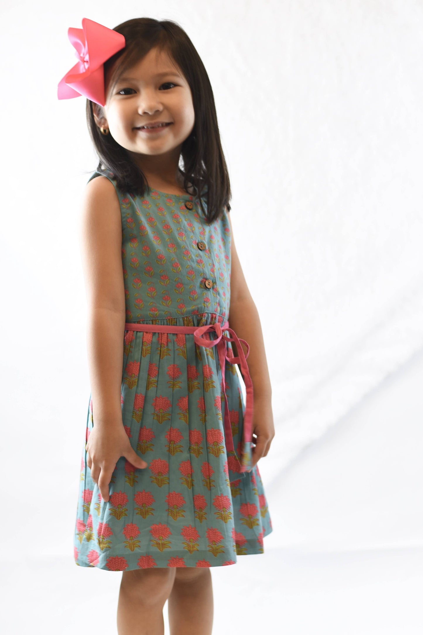 Young girl wearing a patterned dress with a pink bow on a white background