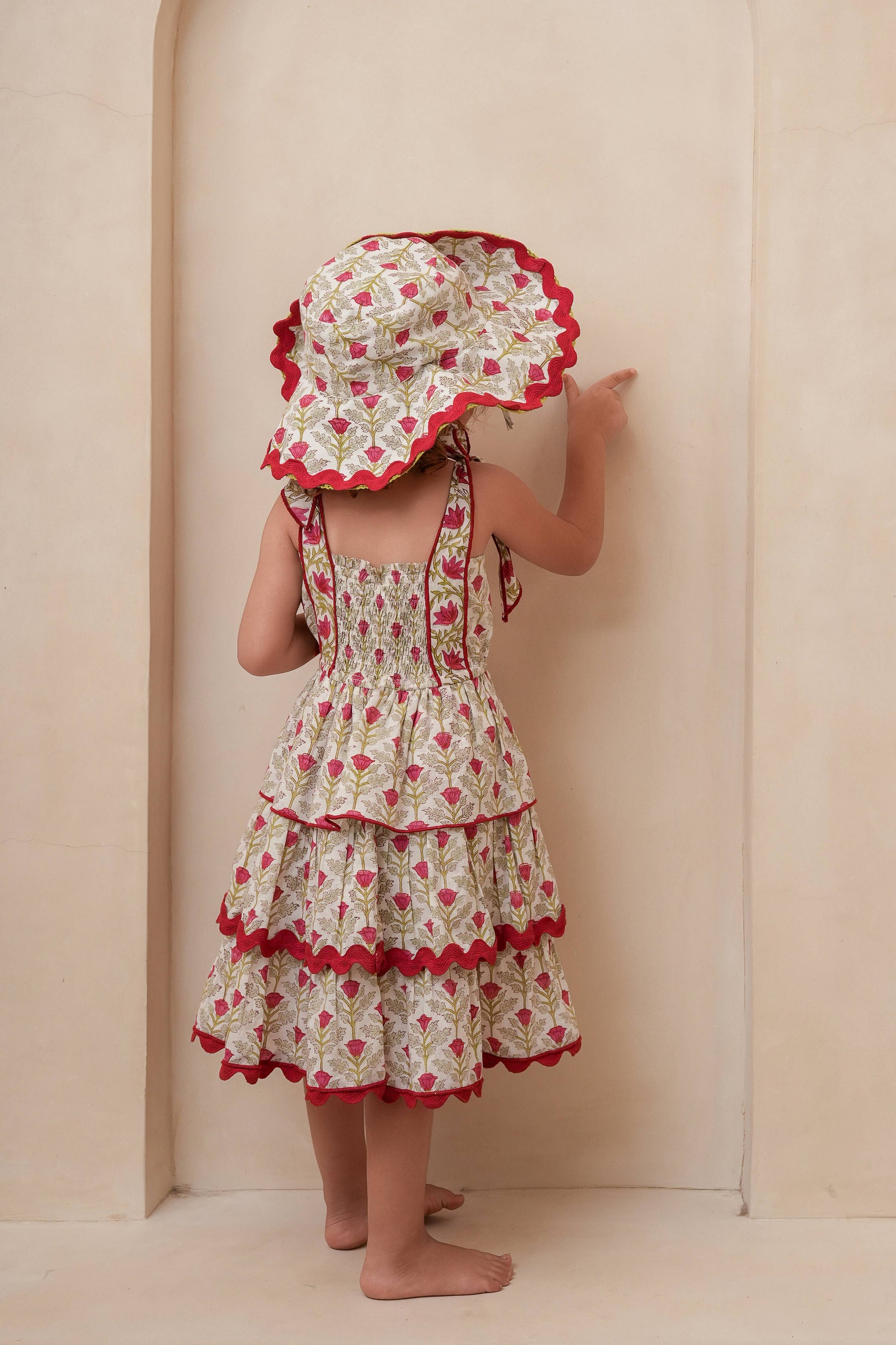 Child wearing a floral dress and hat against a beige wall