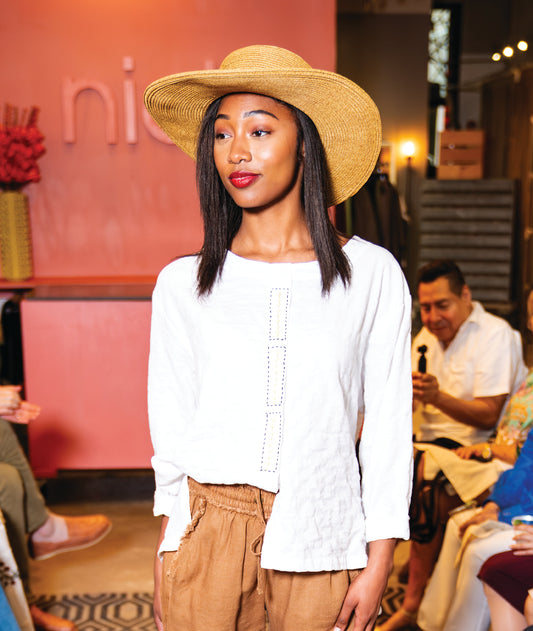 model in brown shorts with a white textured blouse with a large check texture. long sleeves slightly rolled, round neckline, and a floral embroidery along the front placket