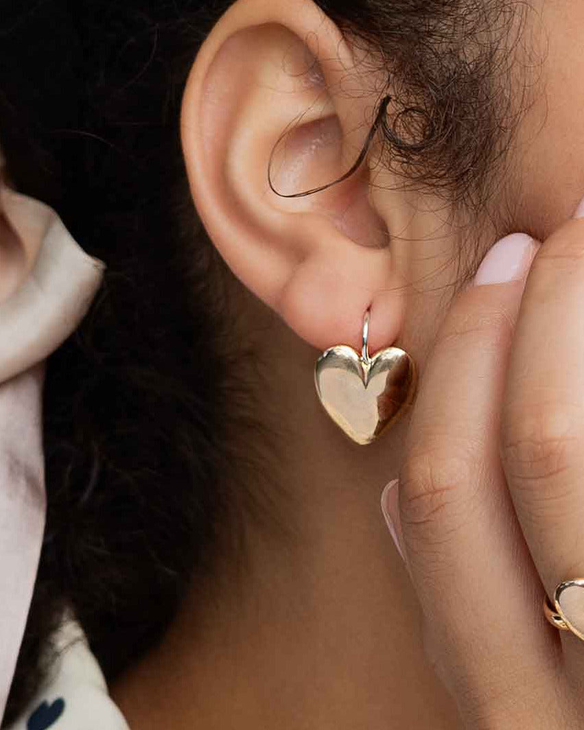 Woman wearing heart-shaped earrings and a ring, with a blurred background