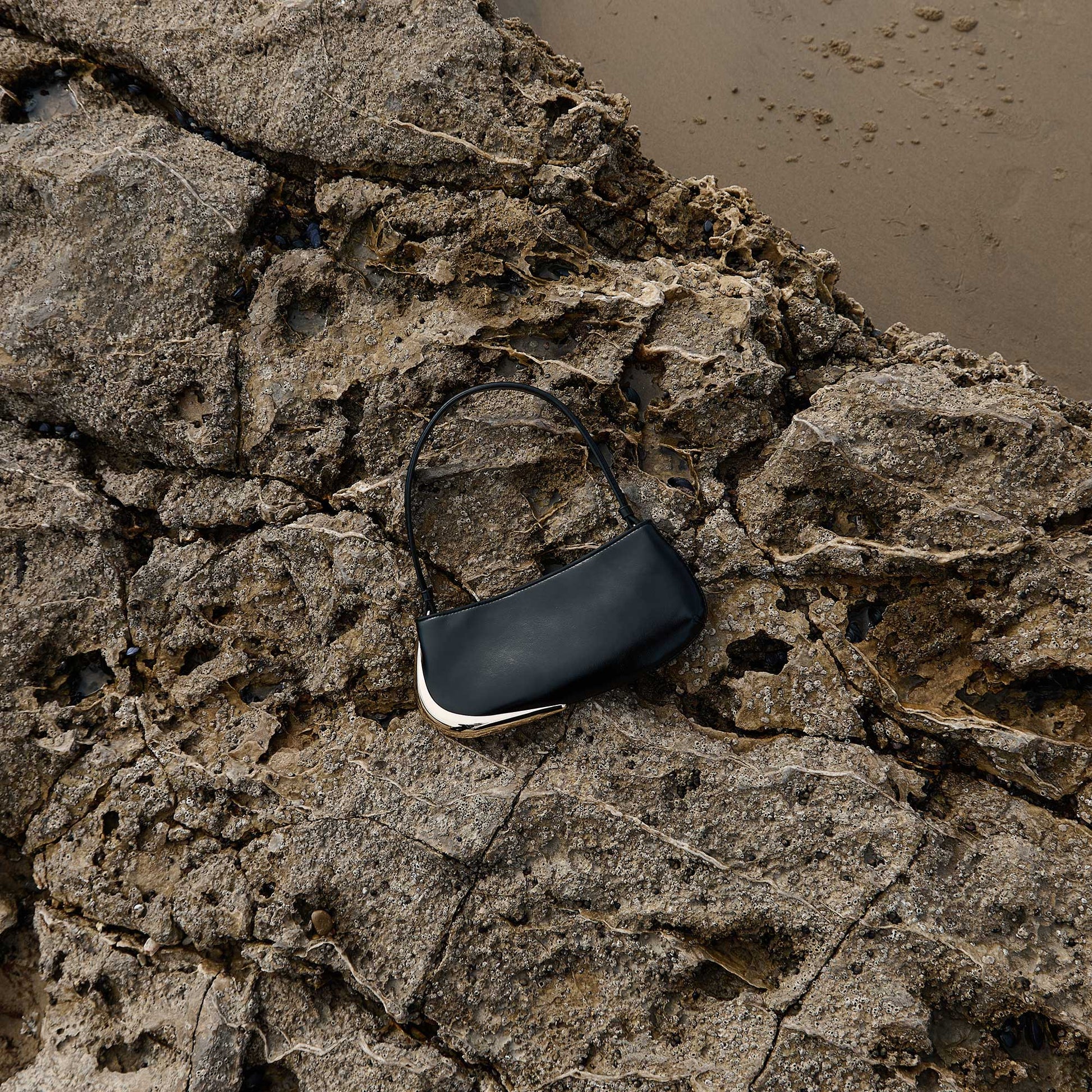 Black handbag with gold accent on a rocky surface