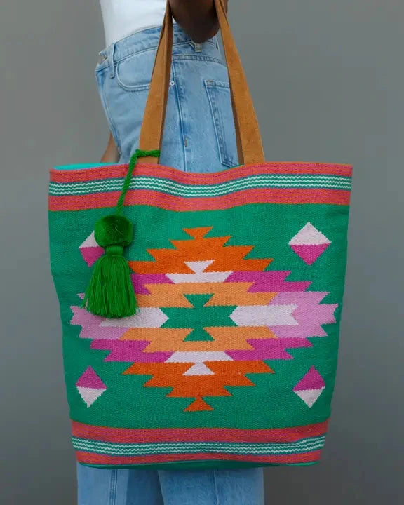 Colorful patterned tote bag held by a person against a gray background