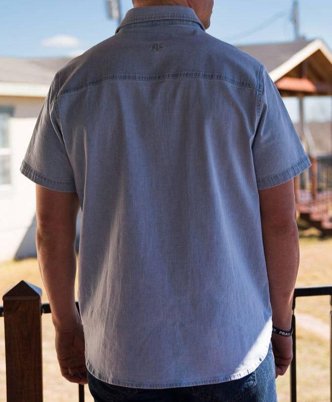 back view of male model wearing short sleeve light blue denim pearl snap shirt outdoors