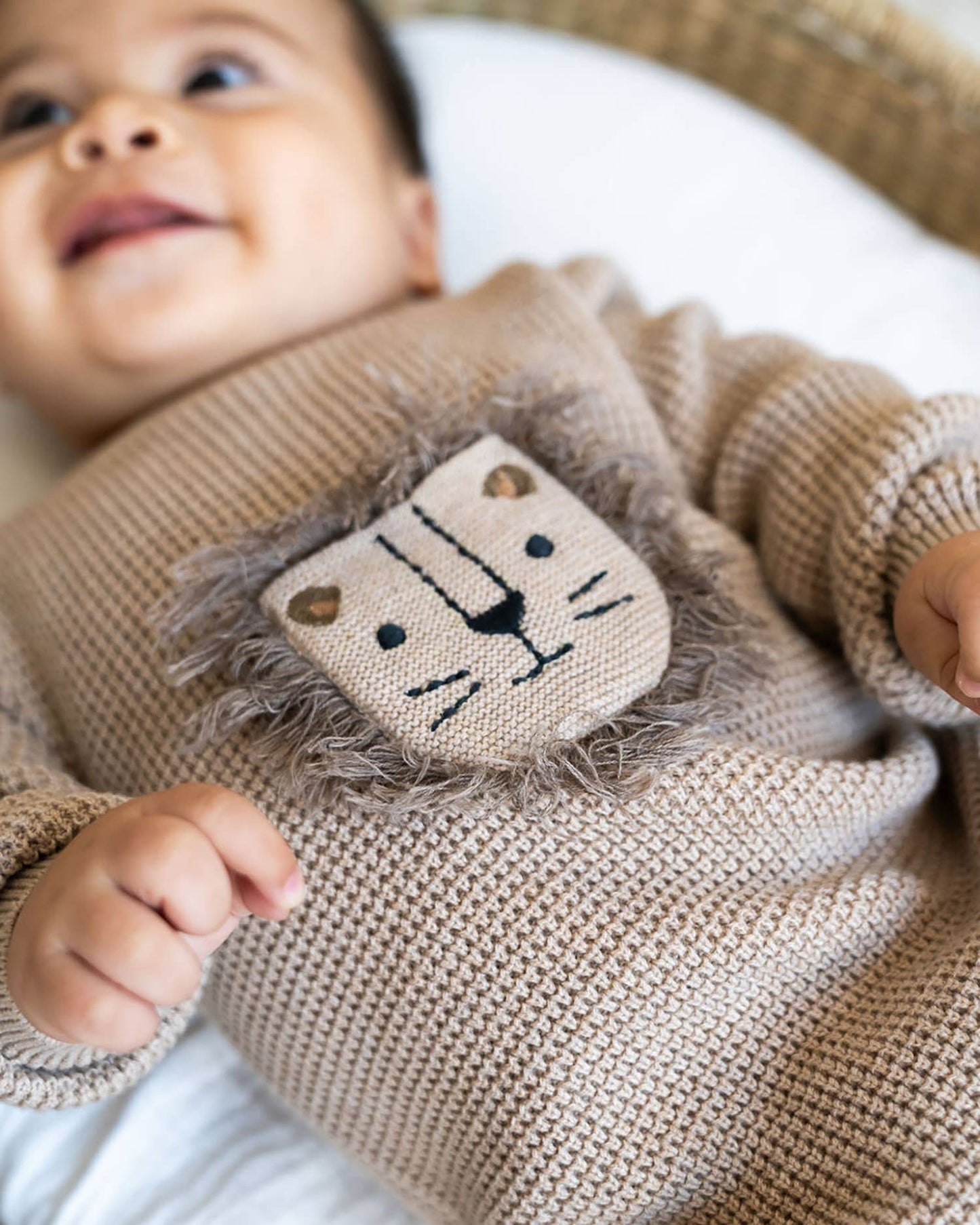 close up of baby wearing light brown baby sweater with lion 3D embroidery and a front pocket