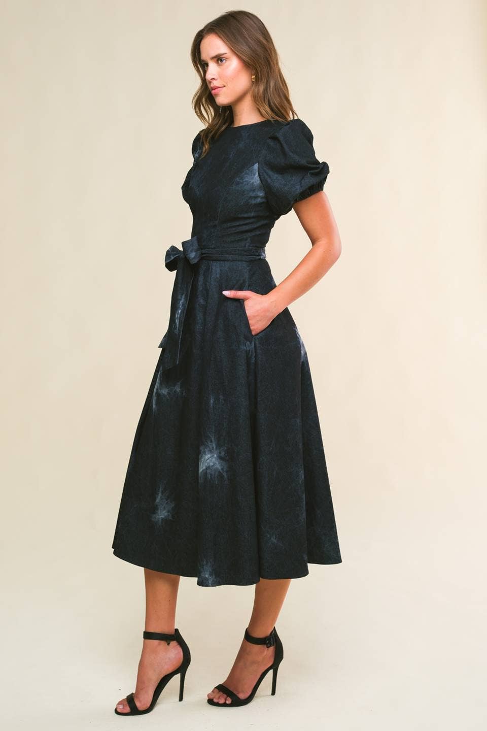 model wearing a twill washed black denim midi dress with round neckline, short puff sleeve, sash tie, full skirt and back zipper closure.