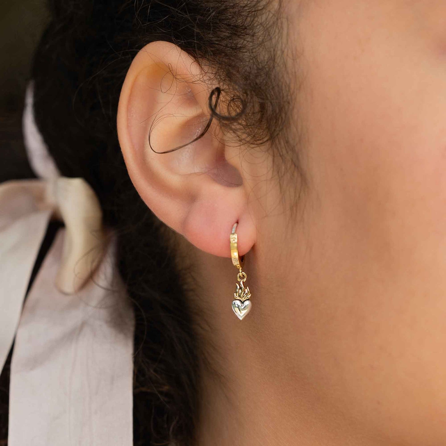 Close-up of an ear wearing a gold earring with a heart charm.