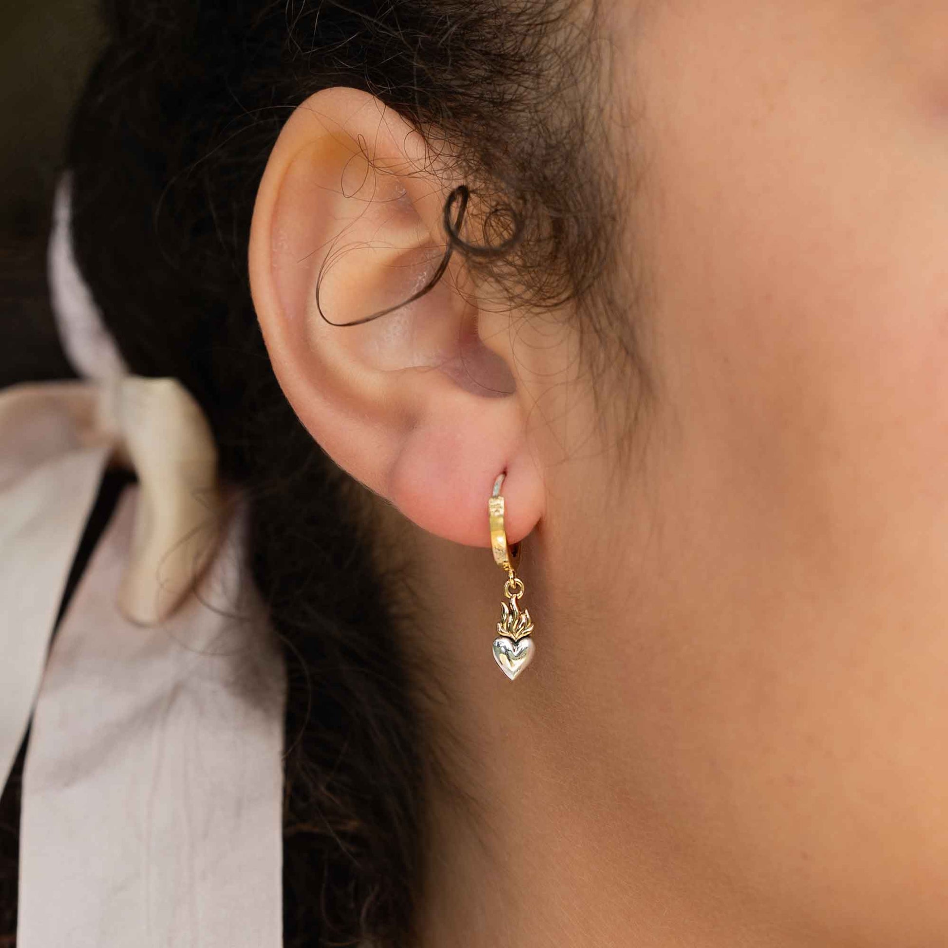 Close-up of an ear wearing a gold earring with a heart charm.