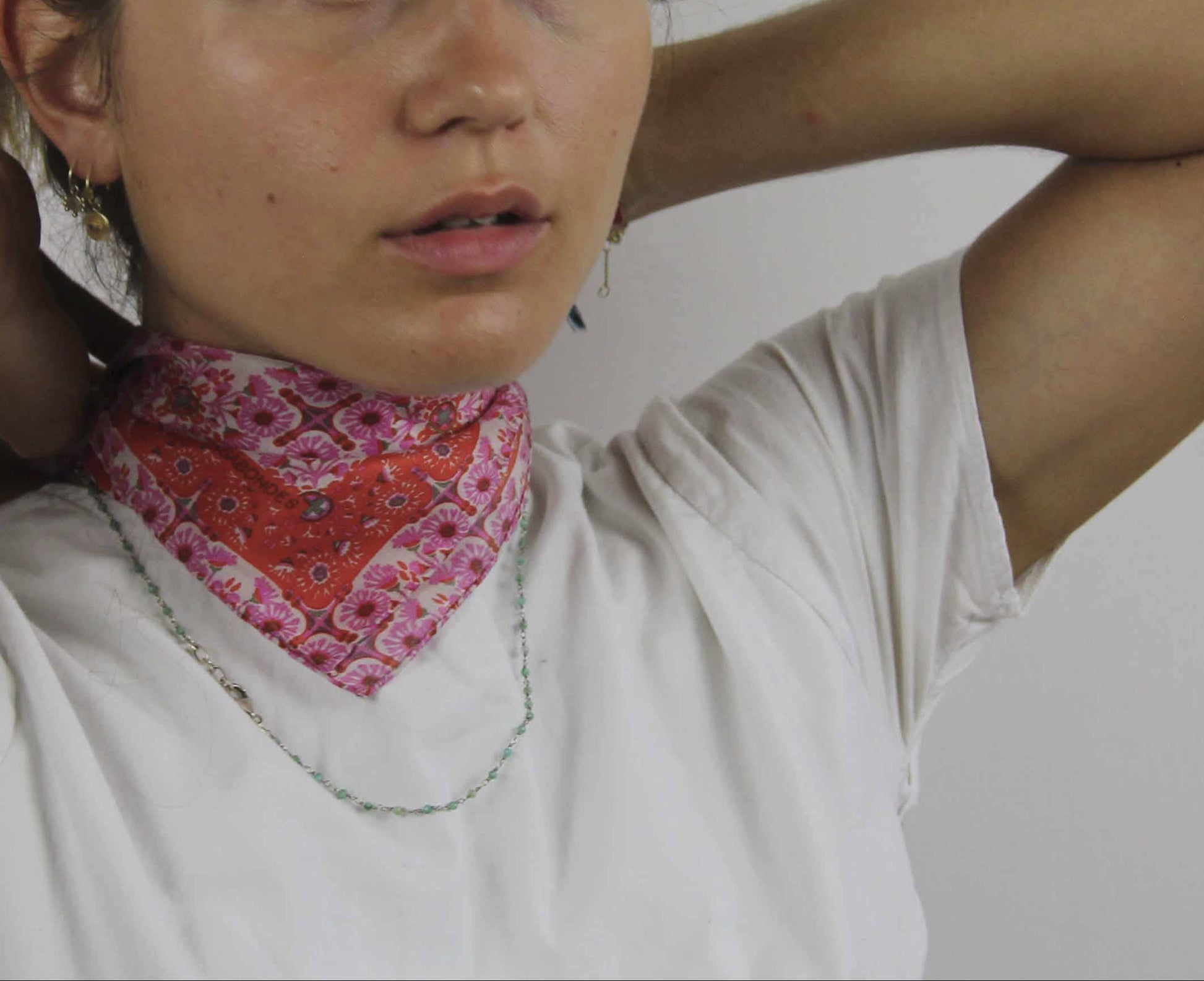 Person wearing a white shirt and red patterned bandana with a plain background