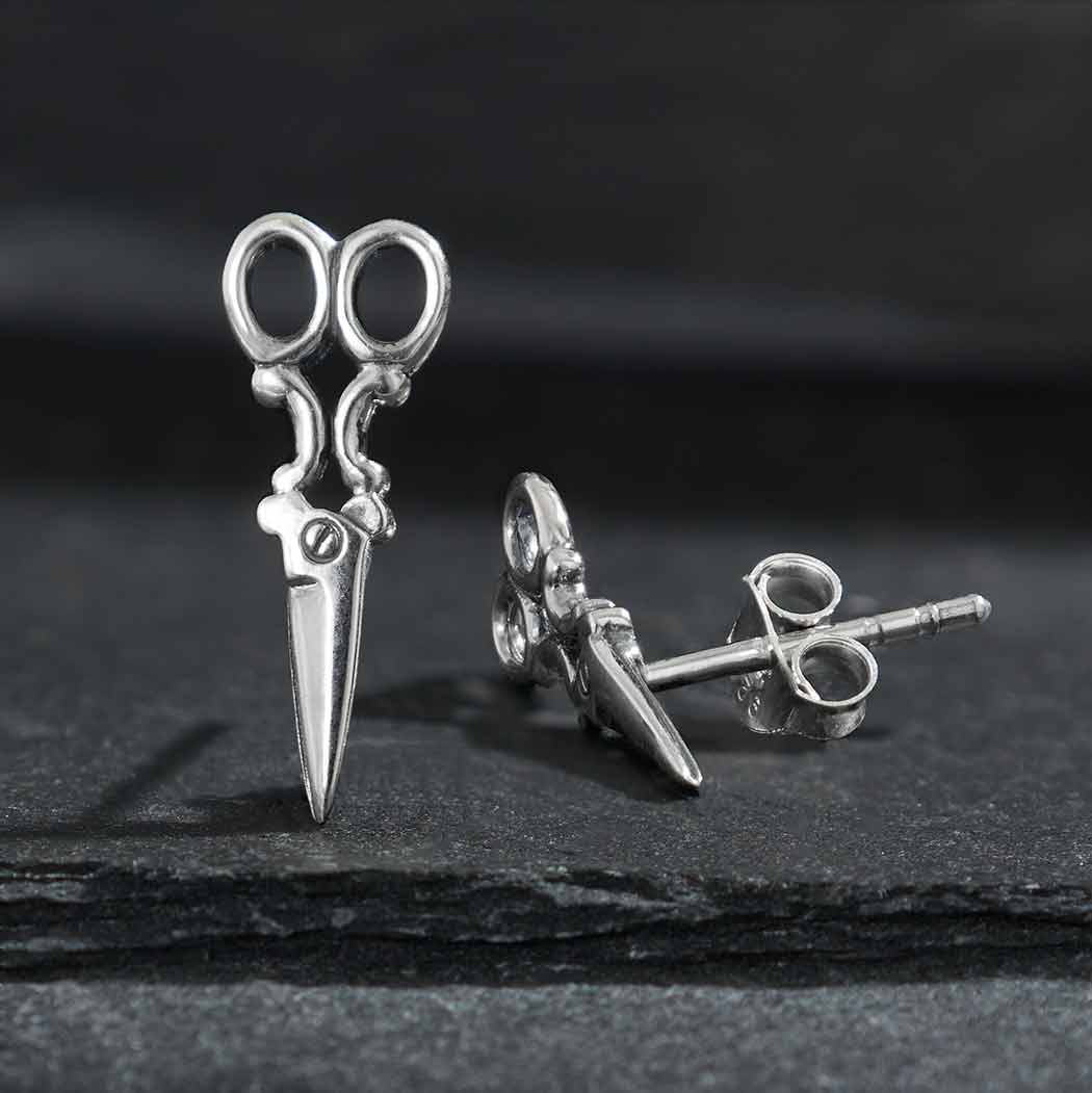 A pair of sterling silver scissor earrings with shearing blades, placed on a dark surface.