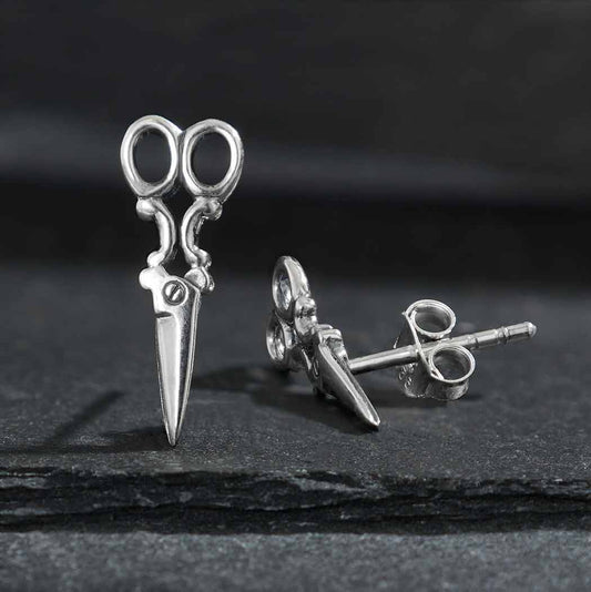 A pair of sterling silver scissor earrings with shearing blades, placed on a dark surface.