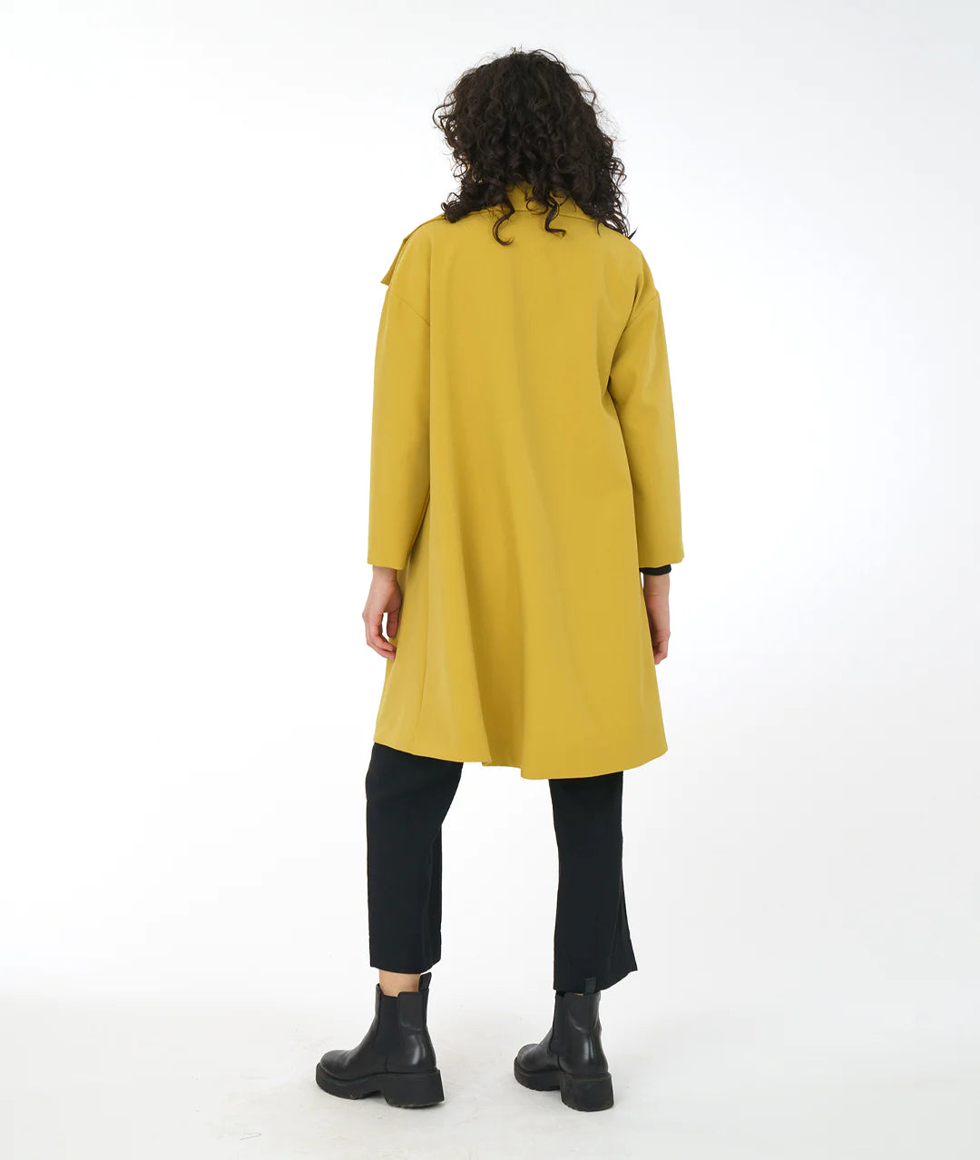 back of model in black pants and boots with a gold asymmetrical jacket with a large collar