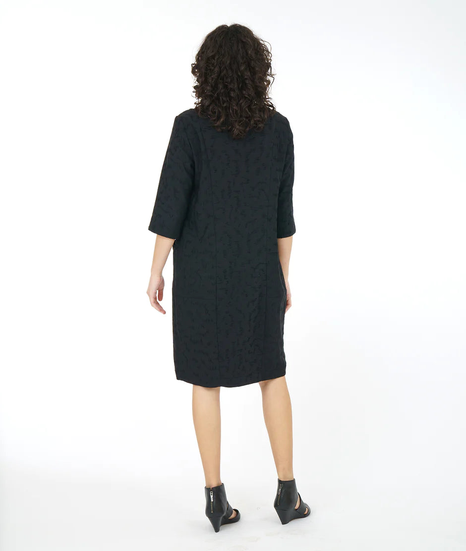back view of model wearing a loose black dress and heeled sandals