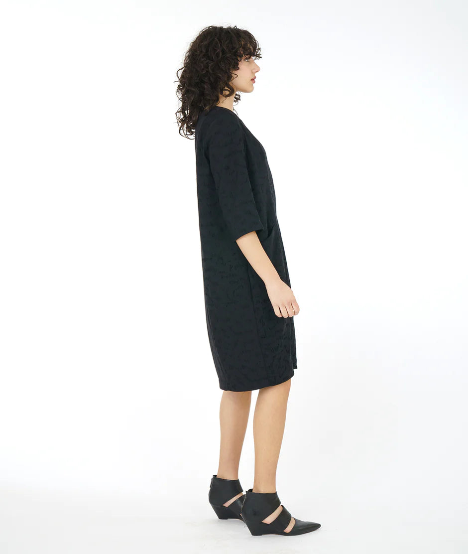 side view of model wearing a loose black dress and heeled sandals
