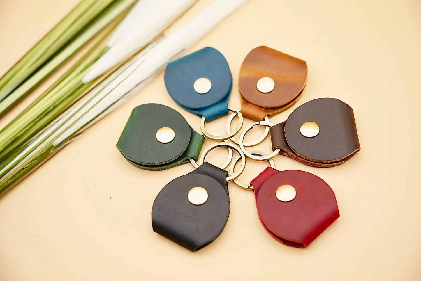 Set of five leather keychains in different colors on a beige surface.
