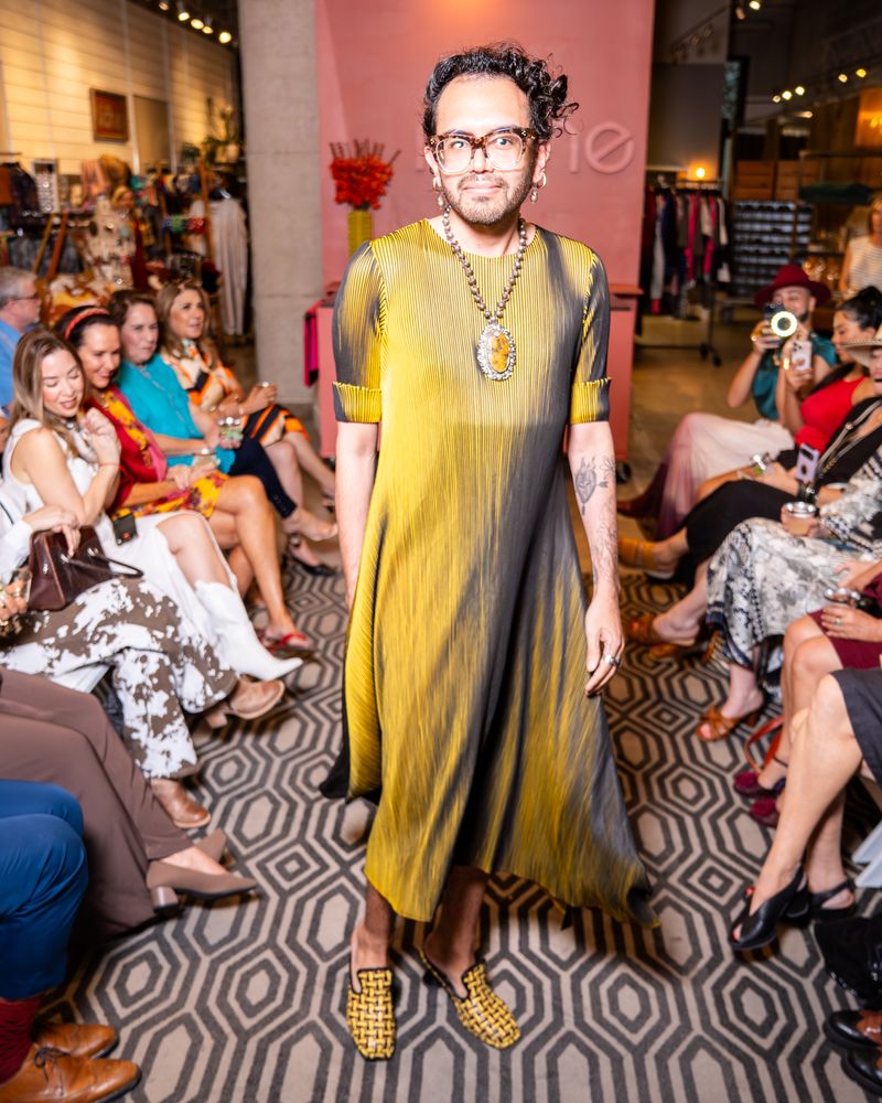 Model in a yellow and black pleated dress walking down a runway