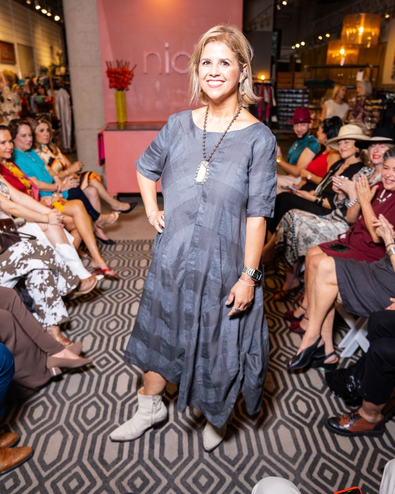model in a dark grey patterned dress, statement earrings and boots walking down a runway
