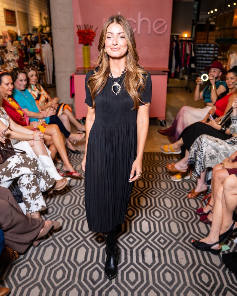 model in a black dress, heart necklace and cowboy boots walking down a runway