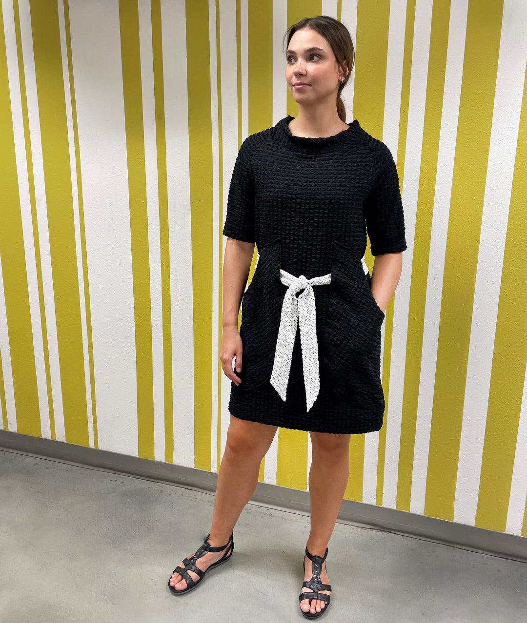 model in a black raglan sleeve shift dress with a white tie belt at the waist, which runs through exterior pocket loops