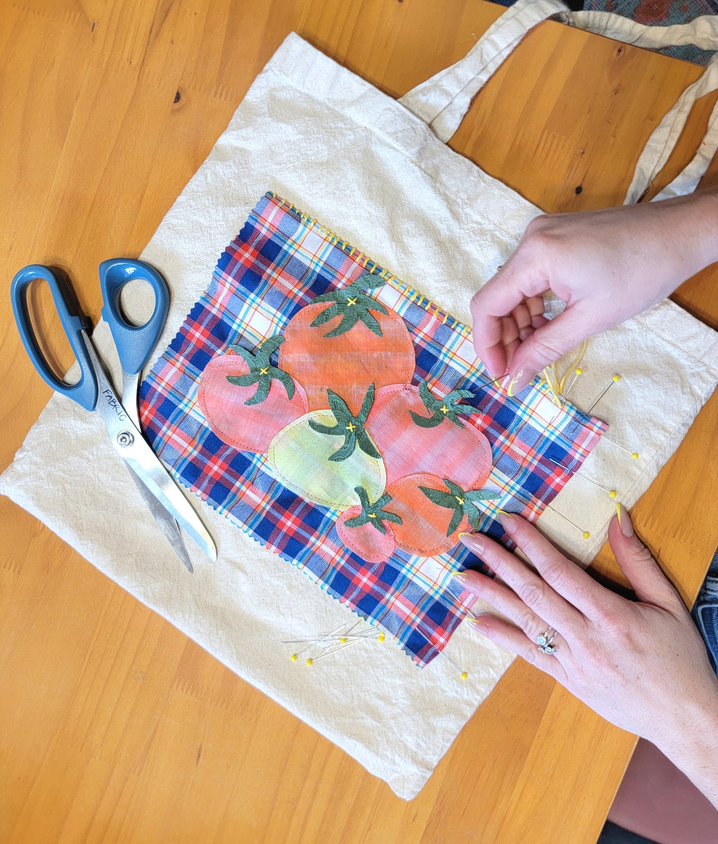 ivory tote bag with a blue and red plaid patch with tomato appliques being hand sewn on to it