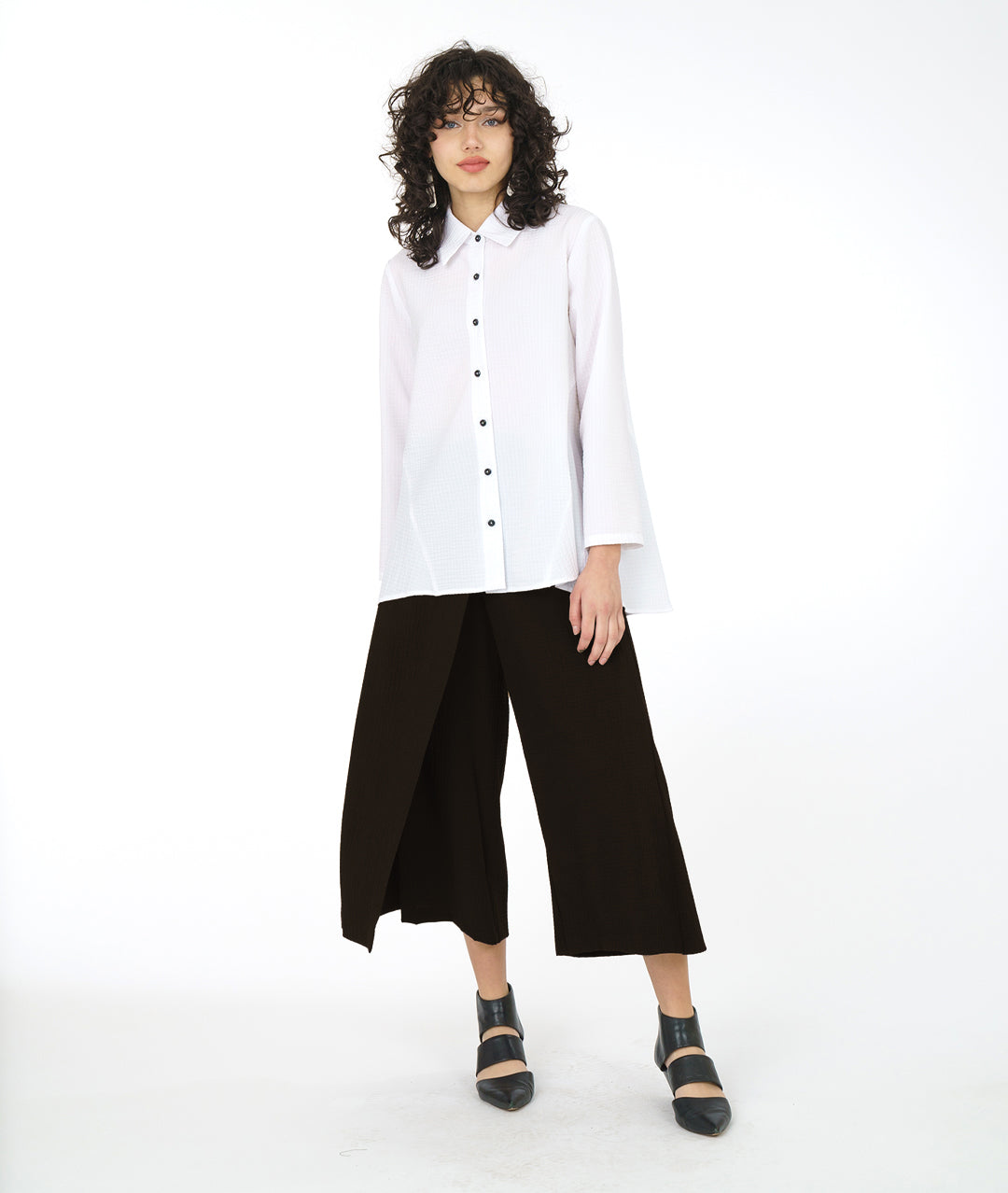 model in a white button down blouse with a wide leg black pant with a skirt like overlay