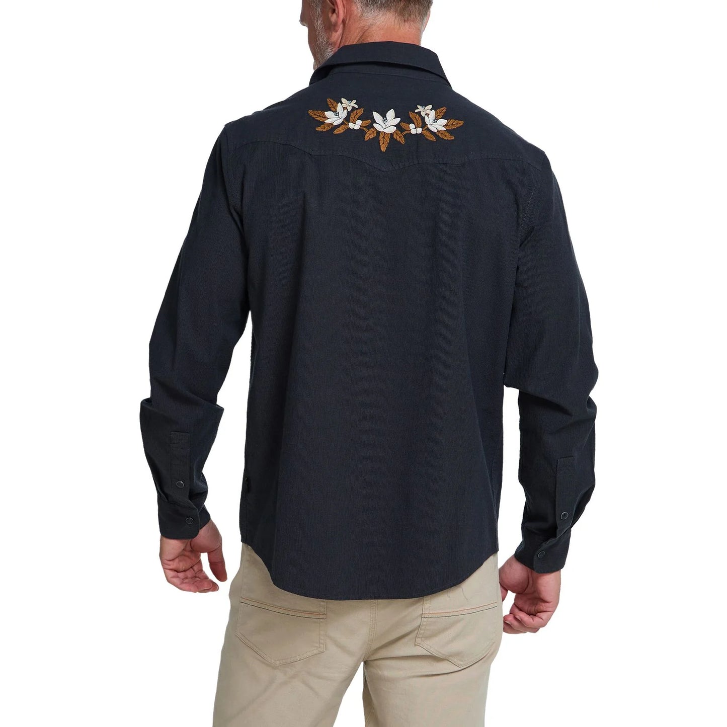 A man viewed from the back wearing a dark long-sleeve western shirt with white and brown floral embroidery across the upper back, paired with khaki pants, on a white background.
