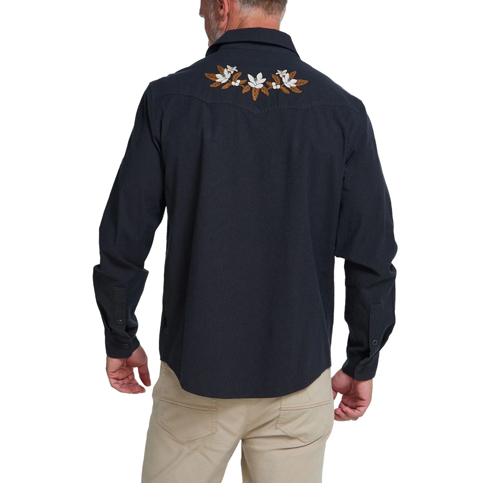 A man viewed from the back wearing a dark long-sleeve western shirt with white and brown floral embroidery across the upper back, paired with khaki pants, on a white background.