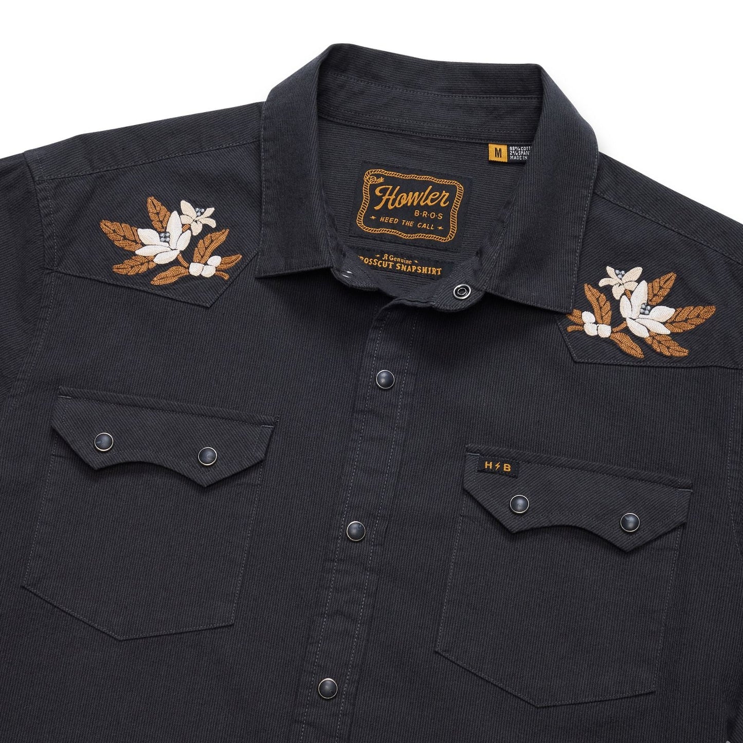 A close-up of a black western-style button-up shirt featuring embroidered floral designs on the shoulders and chest pockets with snap buttons.