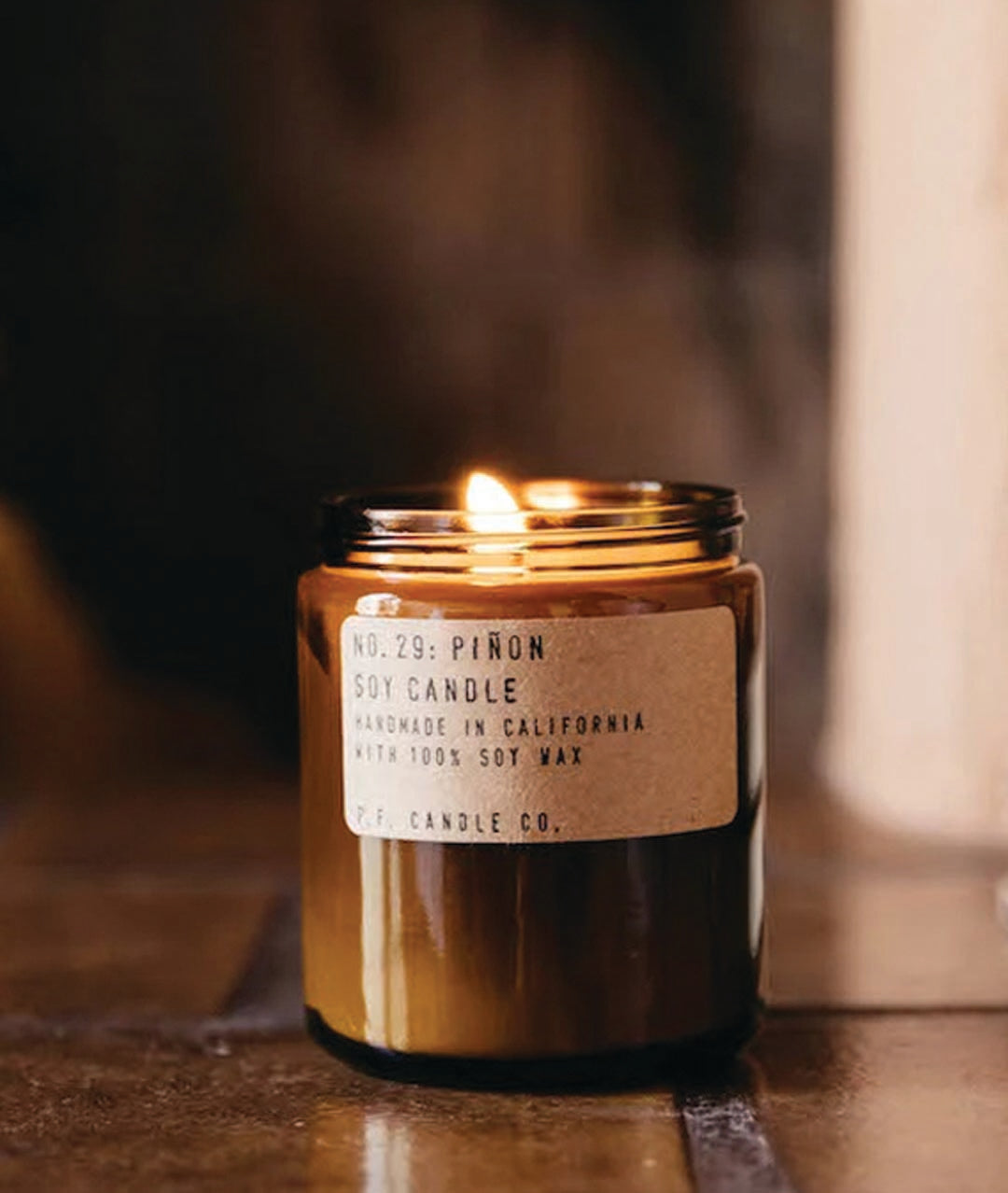 candle encased in an amber colored jar on a brown tiled floor next to books