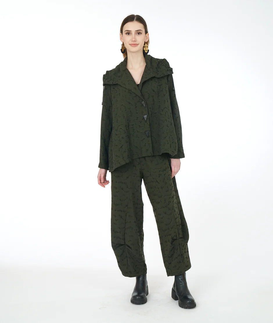 model is wearing an olive green monochromatic outfit with black boots against a white backdrop