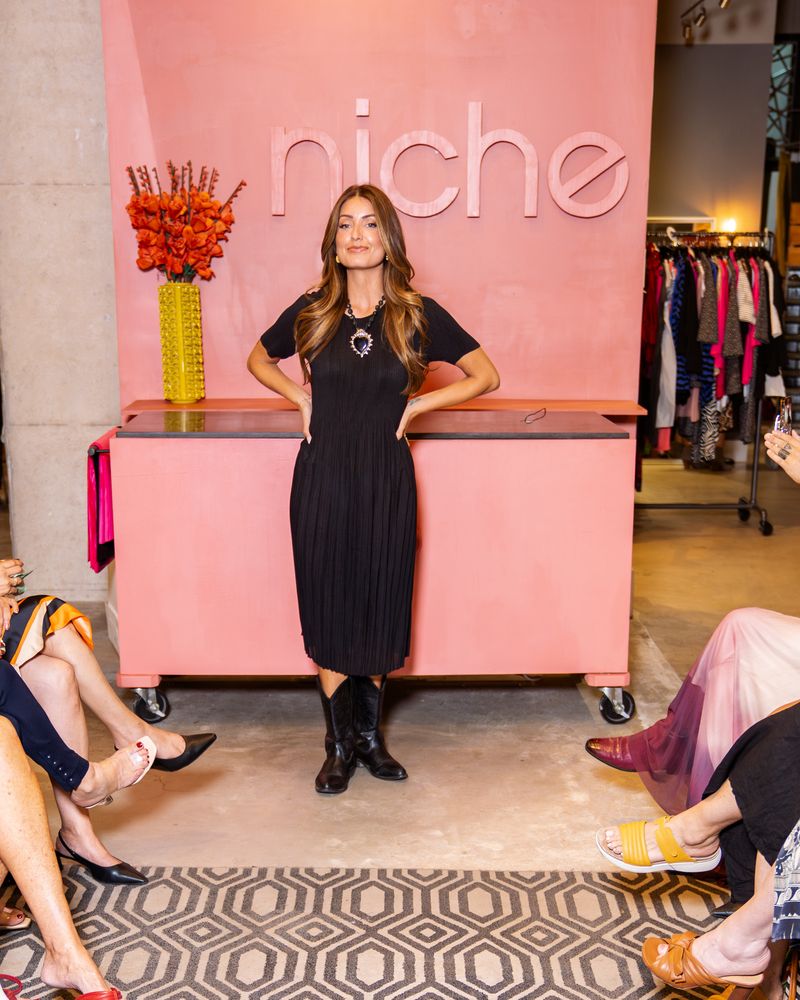 model in a black dress, heart necklace and cowboy boots walking down a runway