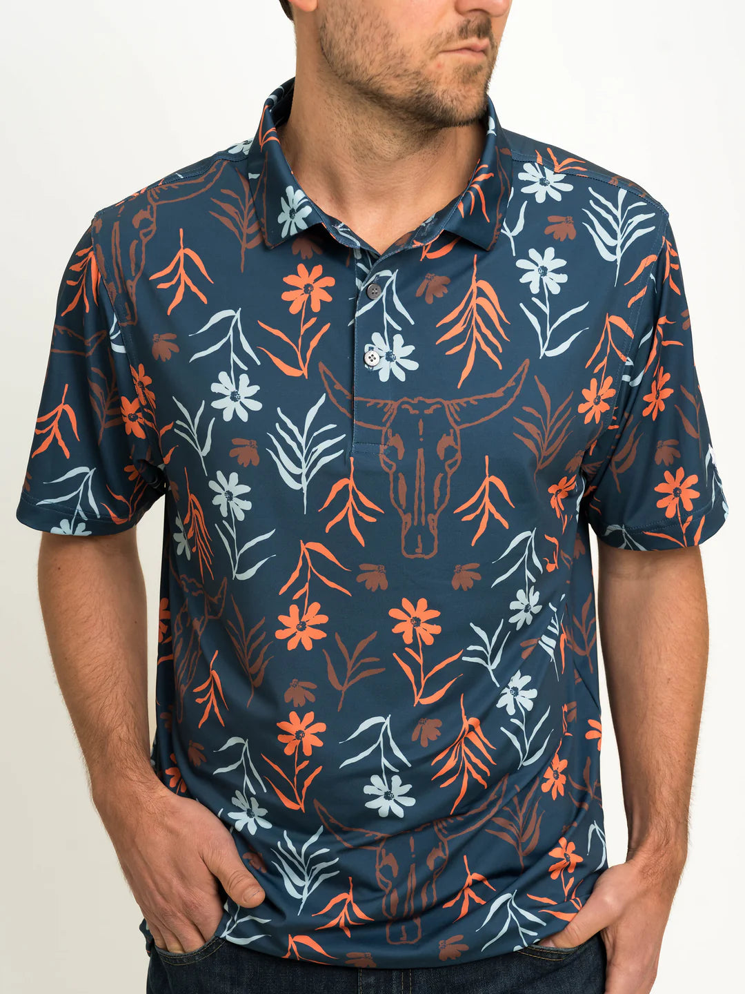 male model wearing a dark blue polo with daisies and cow skulls printed on it