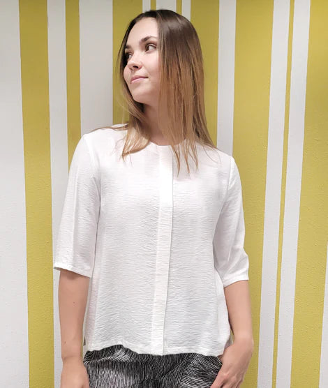 model is wearing a white pullover blouse with a panel down the middle against a striped background