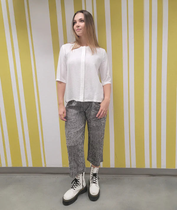 model is wearing a white blouse and black and white striped pants with white combat boots against a striped background